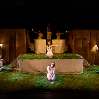 8 actors performing a ritual on moss with lights and water