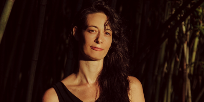 Lola B. Pierson looking at camera with hair swept to one side in black tank top.